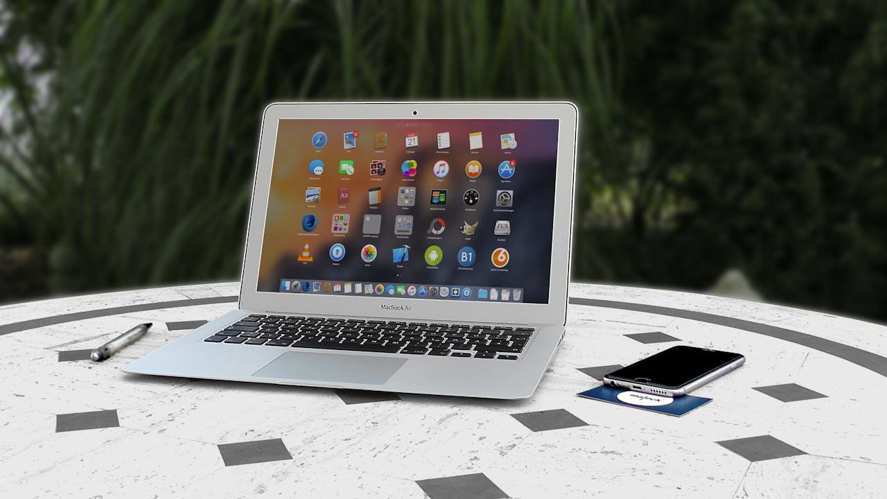 Open laptop with app icons displayed, smartphone and pen on white table outdoors.